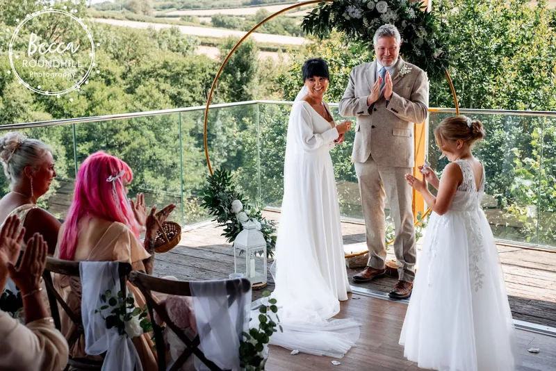 Guests clapping as a couple marry under a gold hoop arch in The Nest